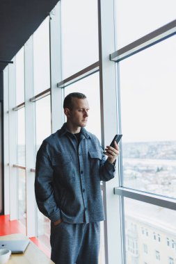 Elinde telefon tutan genç bir iş adamı. Bir ofis ya da iş merkezinde bir gökdelendeki büyük pencerelere karşı. İş ve kariyer, konsept