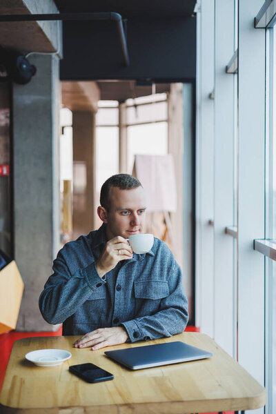 Веселый ИТ-профессионал с ноутбуком разговаривает на смартфоне, чтобы обсудить веб-программирование, счастливый бизнесмен в кафе пьет кофе. фрилансер