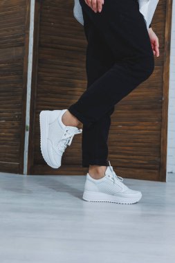 Siyah kotlu, şık, beyaz spor ayakkabılı kadın bacaklarının yakın çekimi. Yeni ayakkabılı şık bir kadın. Modern sezonluk şık spor ayakkabıları koleksiyonu. Kadın modası.