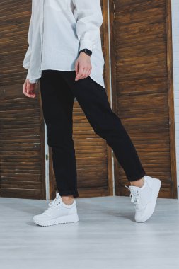 Siyah kotlu, şık, beyaz spor ayakkabılı kadın bacaklarının yakın çekimi. Yeni ayakkabılı şık bir kadın. Modern sezonluk şık spor ayakkabıları koleksiyonu. Kadın modası.