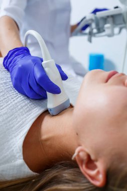 Modern bir kliniğin tıp merkezinde kadın hasta resepsiyonu nitelikli bir uzman ve sağlık sorunları hakkında tavsiyelerde bulunuyor. Tiroit bezinin ultrason muayenesi.