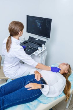 Modern bir kliniğin tıp merkezinde kadın hasta resepsiyonu nitelikli bir uzman ve sağlık sorunları hakkında tavsiyelerde bulunuyor. Tiroit bezinin ultrason muayenesi.