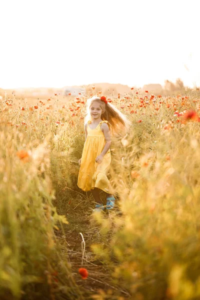 黄色のドレスの女の子は 緑の草の背景に赤いケシの花で実行されます — ストック写真