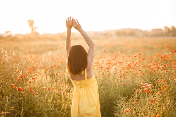 夏の日にケシ畑を歩く黄色のドレスの美しい若い女性 田舎で花を楽しむ少女 選択的焦点 — ストック写真