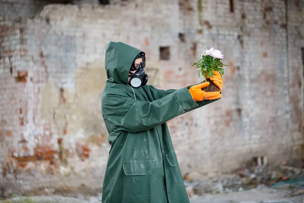 A dosimetrist scientist radiation inspector in protective clothing and a gas mask examines the danger zone. Close-up. Flower. Ecological catastrophy