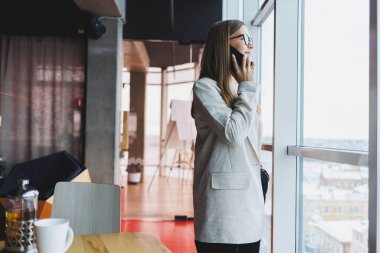 Elinde modern bir akıllı telefon aleti tutan çekici bir kadın düşünceli ve hayalperest görünüyor, cep telefonu tutuyor, sosyal medya paylaşımı için bir fikir üretiyor.