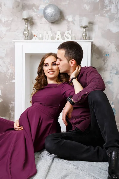 一个怀孕的黑发女人和一个快乐的丈夫正坐在一张三重奏上遥望远方快乐的母爱 灰色混凝土墙和灰色软扶手椅 — 图库照片
