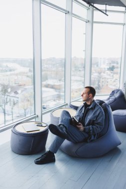 Rahat bir puf üzerinde dinlenen rahat bir takım elbiseli genç bir erkek öğrenci bir not defterine notlar alır. Takım elbiseli çekici bir serbest yazar uzaktan çalışır.