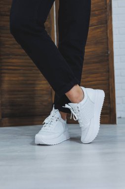 Siyah kotlu, şık, beyaz spor ayakkabılı kadın bacaklarının yakın çekimi. Yeni ayakkabılı şık bir kadın. Modern sezonluk şık spor ayakkabıları koleksiyonu. Kadın modası.