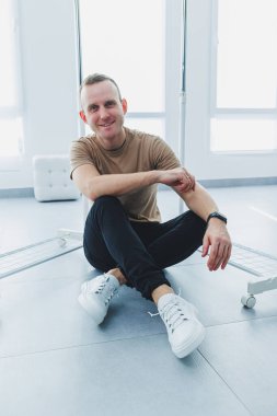 Şık bir genç adam, bej bir tişört ve siyah pantolon giyiyor, beyaz deri spor ayakkabılı bir adam..