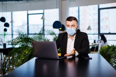 Coronavirus salgını sırasında bir kafede dizüstü bilgisayarla çalışan maskeli yakışıklı bir genç..