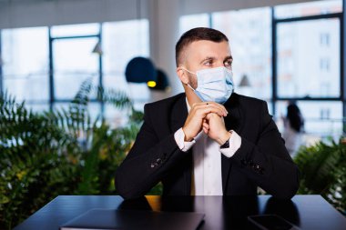 Coronavirus salgını sırasında bir kafede dizüstü bilgisayarla çalışan maskeli yakışıklı bir genç..