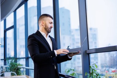 Modern ofis alanındaki büyük pencerelerin yanında oturan başarılı yakışıklı iş adamı.