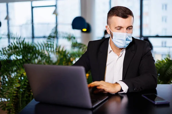 Coronavirus salgını sırasında bir kafede dizüstü bilgisayarla çalışan maskeli yakışıklı bir genç..