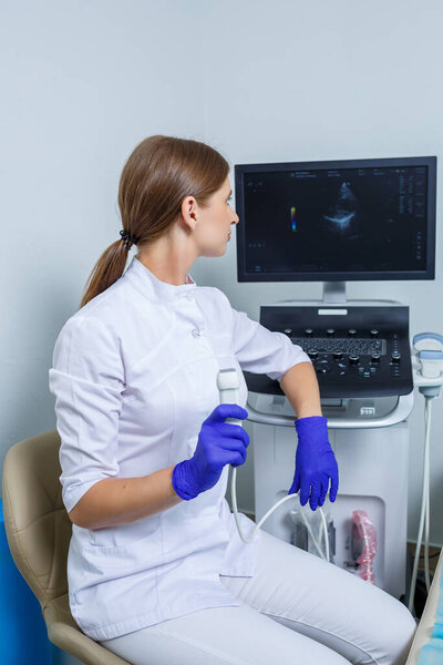 A young woman is an intern doctor, she is in a white suit and medical gloves holding an ultrasound probe on her hands. ultrasound diagnostics. selective focus
