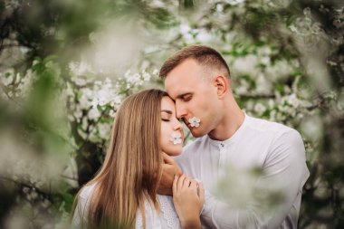 İlkbaharda çiçek açan elma bahçesinde yürüyen genç bir çift. Mutlu evli çift bahçede yürürken eğleniyor. Kadının elini tutan adam.