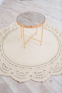 Örülmüş bir pamuk halı ve dekoratif yuvarlak bir masa iç kısmın zeminine karşı yerde yatıyordu. El işi. Bej el yapımı halı.