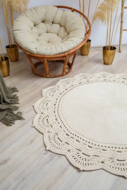 El yapımı, kalın ipliklerden yapılmış ev yapımı halı: bej ipliklerden yapılmış el yapımı halı oturma odasında, koltuğun yanında, örgü sanatının yanında yatıyor.