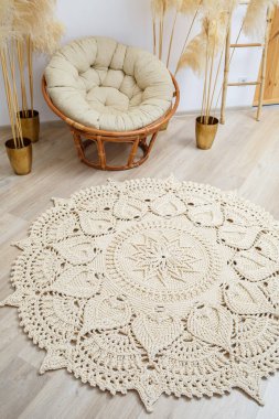 El yapımı, kalın ipliklerden yapılmış ev yapımı halı: bej ipliklerden yapılmış el yapımı halı oturma odasında, koltuğun yanında, örgü sanatının yanında yatıyor.