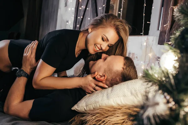 ガーランドと家で新年の前に情熱的なロマンチックなカップルの支出のトップビュー 金髪の若い女性とハンサムな男がベッドの上に横たわっていて 抱き合ってキスしています クリスマスタイム — ストック写真