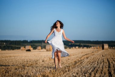 Beyaz bir yaz elbisesi içinde genç ve güzel bir kadın biçilmiş buğday tarlasında duruyor. Kocaman saman demetleriyle, doğanın tadını çıkarıyor. Köyün doğası. Seçici odak