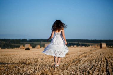 Beyaz bir yaz elbisesi içinde genç ve güzel bir kadın biçilmiş buğday tarlasında duruyor. Kocaman saman demetleriyle, doğanın tadını çıkarıyor. Köyün doğası. Seçici odak