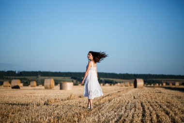 Beyaz bir yaz elbisesi içinde genç ve güzel bir kadın biçilmiş buğday tarlasında duruyor. Kocaman saman demetleriyle, doğanın tadını çıkarıyor. Köyün doğası. Seçici odak