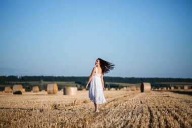 Beyaz bir yaz elbisesi içinde genç ve güzel bir kadın biçilmiş buğday tarlasında duruyor. Kocaman saman demetleriyle, doğanın tadını çıkarıyor. Köyün doğası. Seçici odak