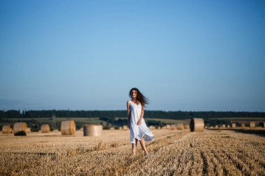Beyaz bir yaz elbisesi içinde genç ve güzel bir kadın biçilmiş buğday tarlasında duruyor. Kocaman saman demetleriyle, doğanın tadını çıkarıyor. Köyün doğası. Seçici odak