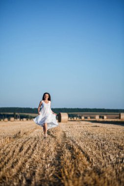 Beyaz bir yaz elbisesi içinde genç ve güzel bir kadın biçilmiş buğday tarlasında duruyor. Kocaman saman demetleriyle, doğanın tadını çıkarıyor. Köyün doğası. Seçici odak