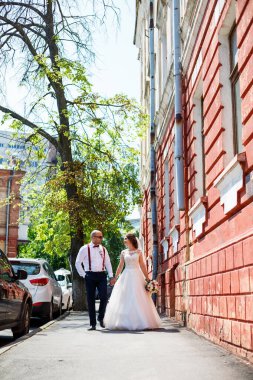 Gelin ve damat gelinlik içinde düğün günü şehir sokaklarında yürüyorlar.