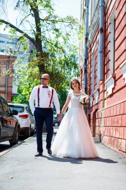 Gelin ve damat gelinlik içinde düğün günü şehir sokaklarında yürüyorlar.