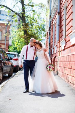 Gelin ve damat gelinlik içinde düğün günü şehir sokaklarında yürüyorlar.