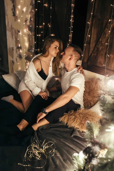 情熱的なカップルは クリスマスツリーの近くのベッドの上に座っている 本当の感情だ 冬の休暇中の快適さの喜びの瞬間 クリスマスロマンチックな気分 — ストック写真