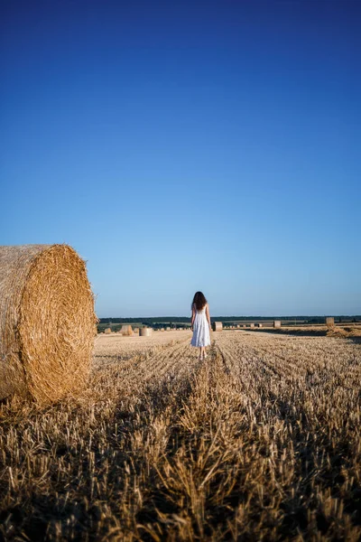 Beyaz bir yaz elbisesi içinde genç ve güzel bir kadın biçilmiş buğday tarlasında duruyor. Kocaman saman demetleriyle, doğanın tadını çıkarıyor. Köyün doğası. Seçici odak