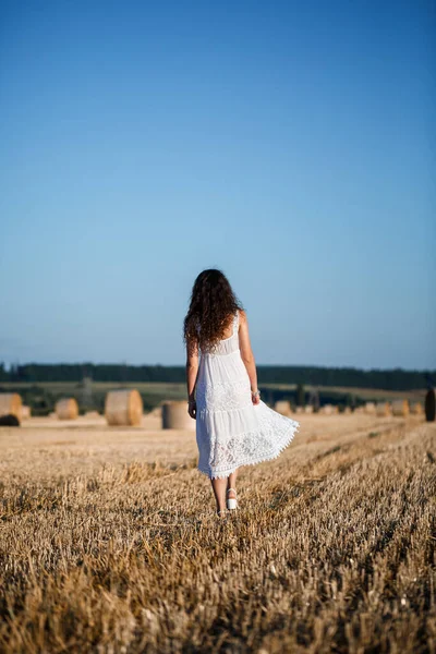 Beyaz bir yaz elbisesi içinde genç ve güzel bir kadın biçilmiş buğday tarlasında duruyor. Kocaman saman demetleriyle, doğanın tadını çıkarıyor. Köyün doğası. Seçici odak