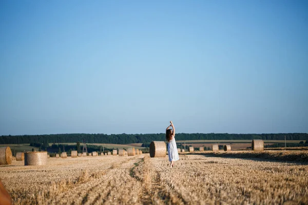 Beyaz bir yaz elbisesi içinde genç ve güzel bir kadın biçilmiş buğday tarlasında duruyor. Kocaman saman demetleriyle, doğanın tadını çıkarıyor. Köyün doğası. Seçici odak