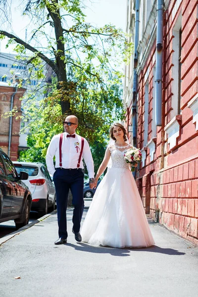 Gelin ve damat gelinlik içinde düğün günü şehir sokaklarında yürüyorlar.