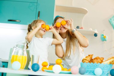 Genç bir anne ve kız mutfakta taze turunçgillerle oynuyorlar, yüzlerinde gözler yerine mandalinalar. Bir çocukla aile ilişkisi