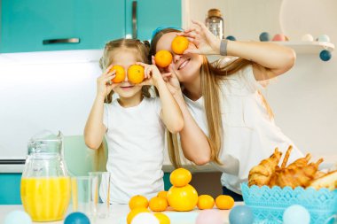 Genç bir anne ve kız mutfakta taze turunçgillerle oynuyorlar, yüzlerinde gözler yerine mandalinalar. Bir çocukla aile ilişkisi