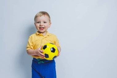3-4 yaşlarında, sarı tişörtlü bir futbol fanatiği elinde bir top, beyaz bir arka planda izole bir futbol topu tutuyor. Spor aile eğlencesi konsepti