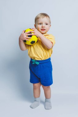 Küçük şirin çocuk bebek çocuk 3-4 yaşında, sarı zemin üzerine kırmızı t-shirt futbol topu elinde tutan futbol fan izole. Çocuklar spor aile eğlence yaşam tarzı kavramı. Kopyalama alanı reklam
