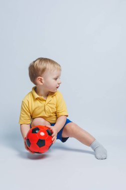 Küçük şirin çocuk bebek çocuk 3-4 yaşında, sarı zemin üzerine kırmızı t-shirt futbol topu elinde tutan futbol fan izole. Çocuklar spor aile eğlence yaşam tarzı kavramı. Kopyalama alanı reklam