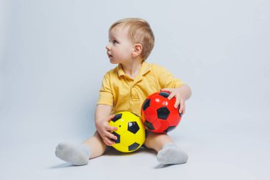 Erkek taraftar elinde bir futbol topu tutuyor, beyaz bir arka planda izole edilmiş. Futboldaki yeni çocuk, çocuklar için spor. Küçük atlet. Çocuklar için sarı ve mavi futbol takımı