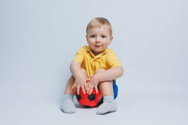 Elinde futbol topu olan sarı tişörtlü küçük bir çocuk beyaz arka planda izole edilmiş bir şekilde gülümsüyor. Spor çocuğu elinde top tutuyor. Çocuk sporları oyunu. Küçük sporcu..
