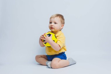 3-4 yaşlarında, sarı tişörtlü bir futbol fanatiği elinde bir top, beyaz bir arka planda izole bir futbol topu tutuyor. Spor aile eğlencesi konsepti