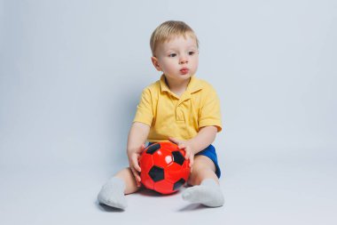 5-6 yaşlarında sarı tişörtlü neşeli bir çocuk, takımı destekliyor, elinde bir futbol topu tutuyor, beyaz bir arka planda izole edilmiş. Spor aile eğlencesi konsepti