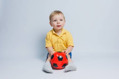 Küçük şirin çocuk bebek çocuk 3-4 yaşında, sarı zemin üzerine kırmızı t-shirt futbol topu elinde tutan futbol fan izole. Çocuklar spor aile eğlence yaşam tarzı kavramı. Kopyalama alanı reklam