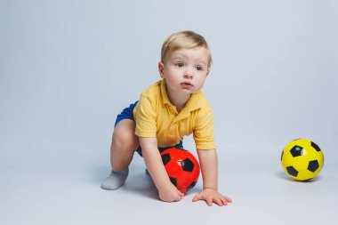 Erkek taraftar elinde bir futbol topu tutuyor, beyaz bir arka planda izole edilmiş. Futboldaki yeni çocuk, çocuklar için spor. Küçük atlet. Çocuklar için sarı ve mavi futbol takımı