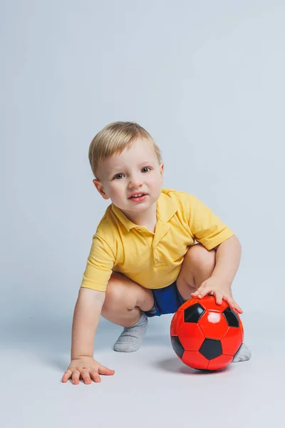 黄色のTシャツの陽気な小さな男の子5 6歳のサッカーファンは チームをサポートし 白い背景に隔離された彼の手の中にサッカーボールを保持しています スポーツファミリーレクリエーションの概念 — ストック写真